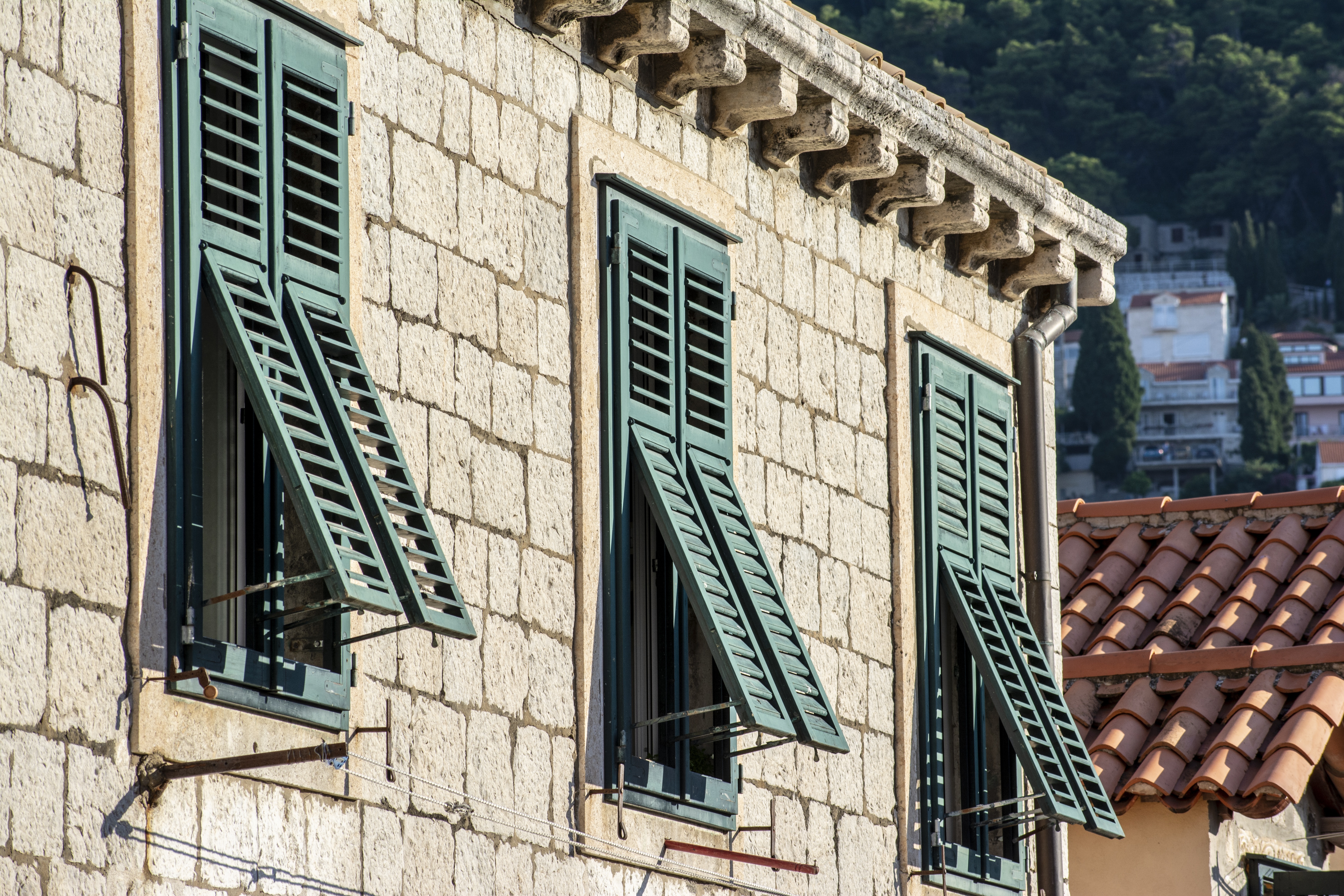 Casa in pietra con persiane verdi aperte e vista sui tetti rossi e sulle colline sullo sfondo.