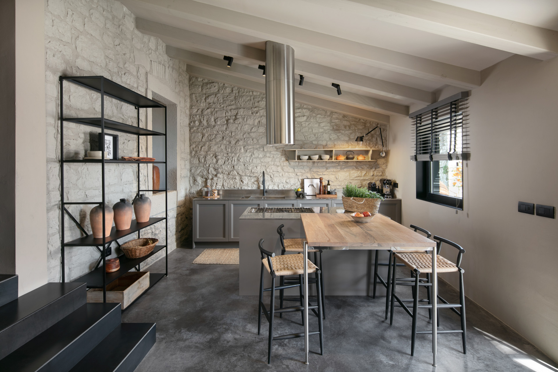 Moderne Küche der Villa IPause mit Steinwand, Holzinsel, Barhockern und offenen Regalen in warmem, minimalistischem Stil.