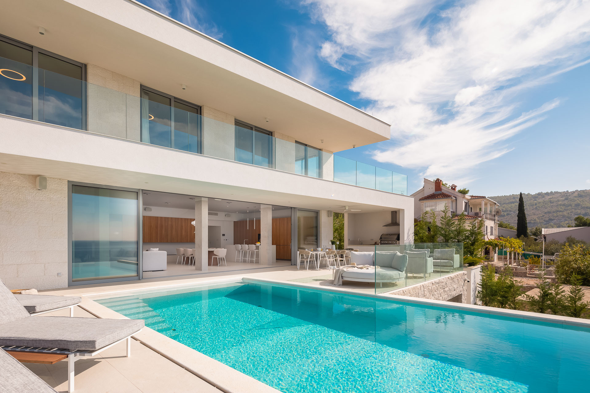 Villa de luxe moderne avec une grande piscine extérieure, des garde-corps en verre et un vaste espace de vie ouvert.