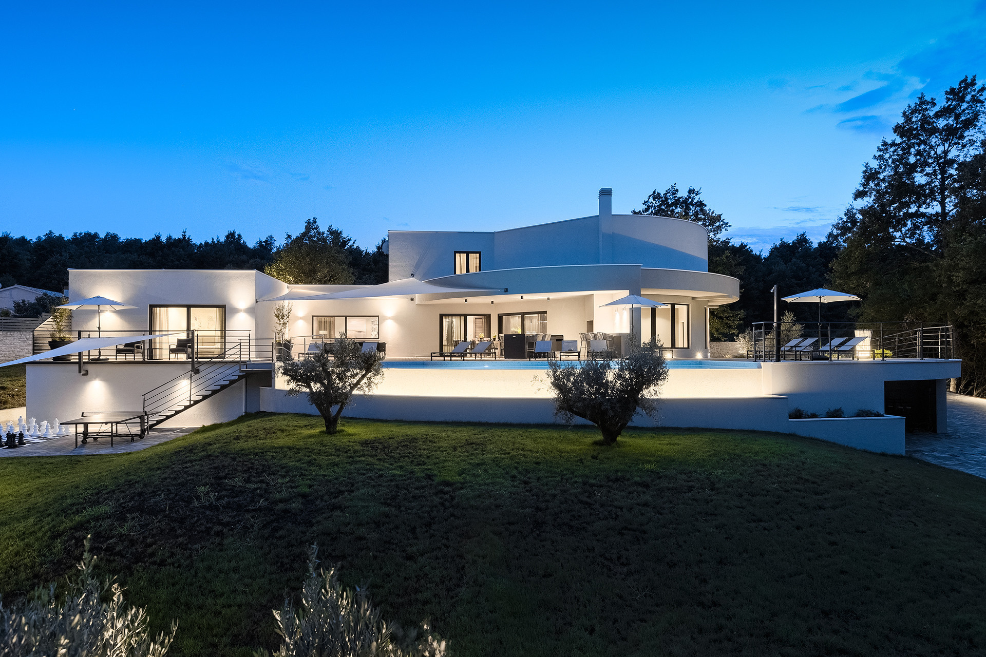 Modern white Villa Viktor Tireli in Istria featuring an illuminated terrace and pool, surrounded by nature and a manicured lawn for intimate weddings.