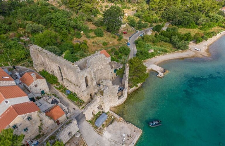 Aerial view of the historic Roman palace ruins in Polače on Mljet Island, surrounded by traditional stone houses and the crystal-clear turquoise Adriatic Sea.