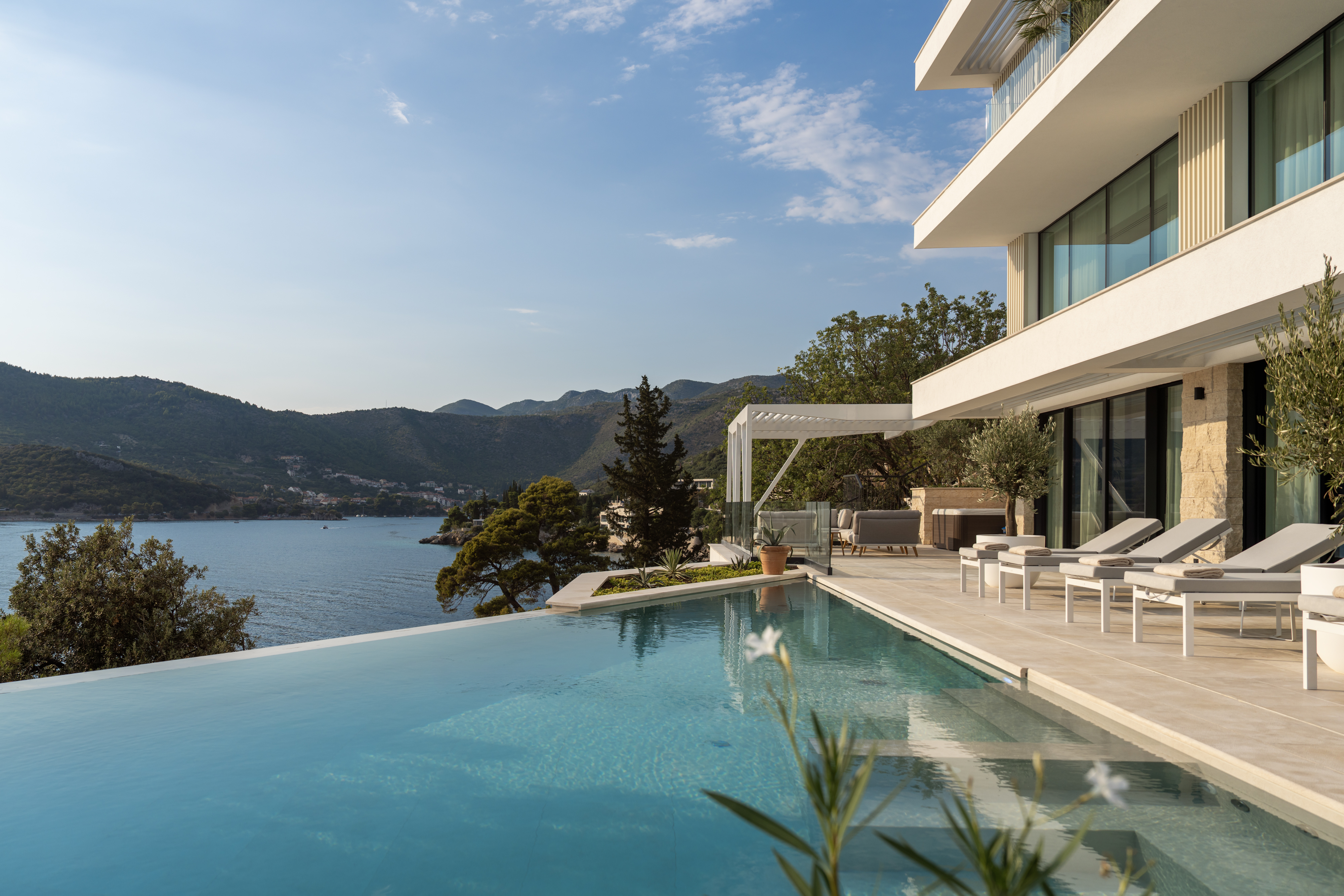illa Klara Dubrovnik featuring a stunning infinity pool, spacious terrace with sun loungers and contemporary architecture overlooking the Adriatic Sea and surrounding green hills.