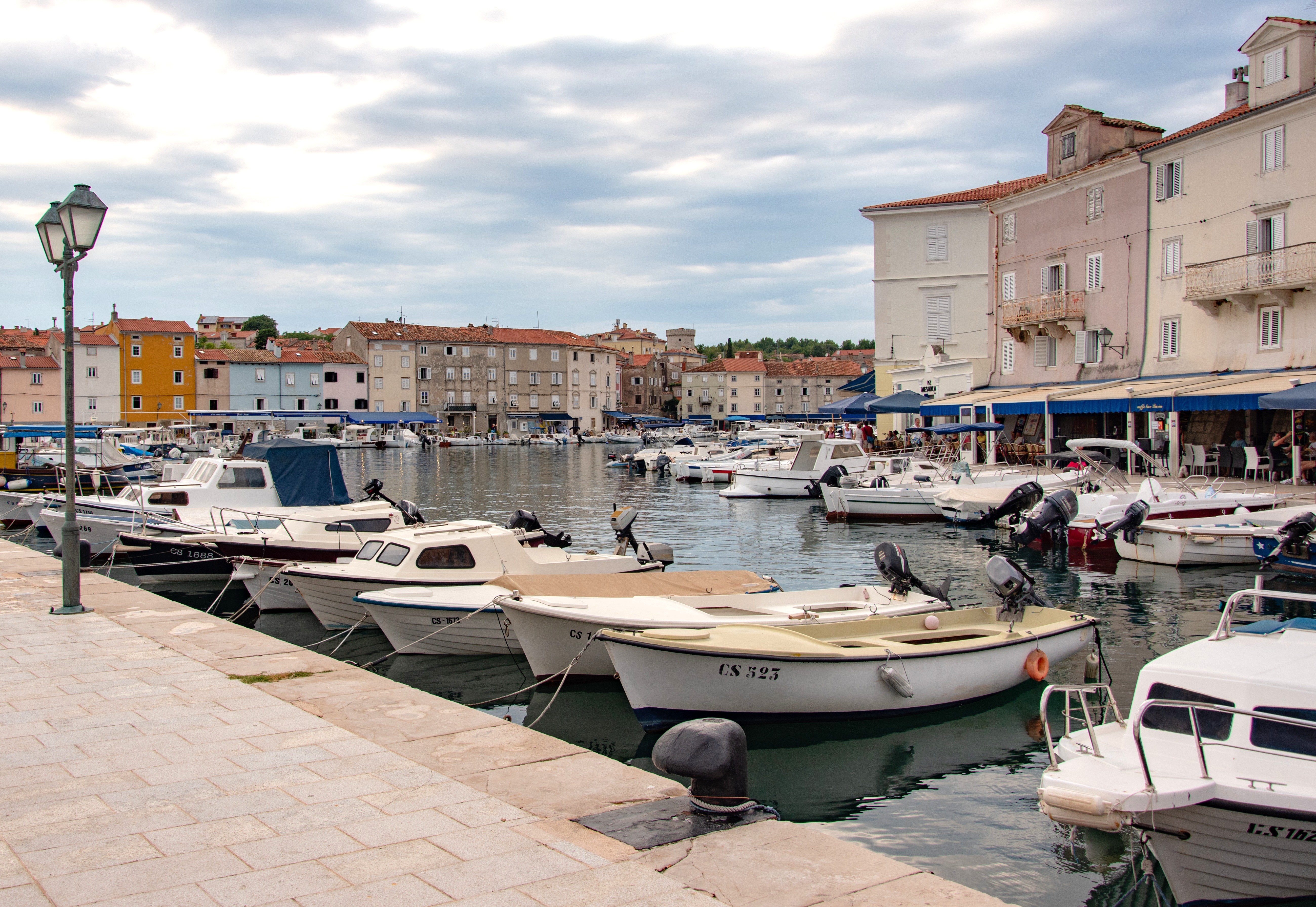 Malowniczy port w miejscowości Cres, z tradycyjnymi łodziami rybackimi, kolorowymi zabytkowymi budynkami i nadbrzeżną promenadą na wyspie Cres w Chorwacji.