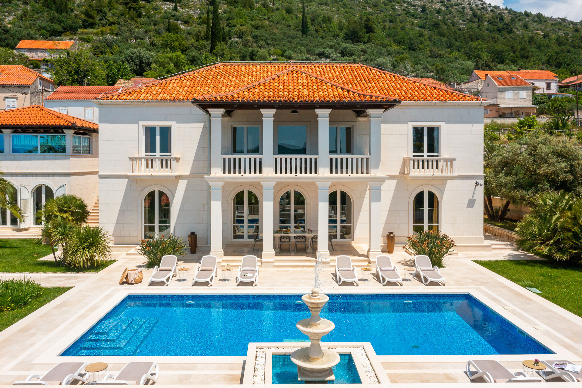 La Villa Dubrovnik featuring elegant Mediterranean architecture, a private swimming pool with a decorative fountain, spacious sun terrace with loungers and a landscaped garden.