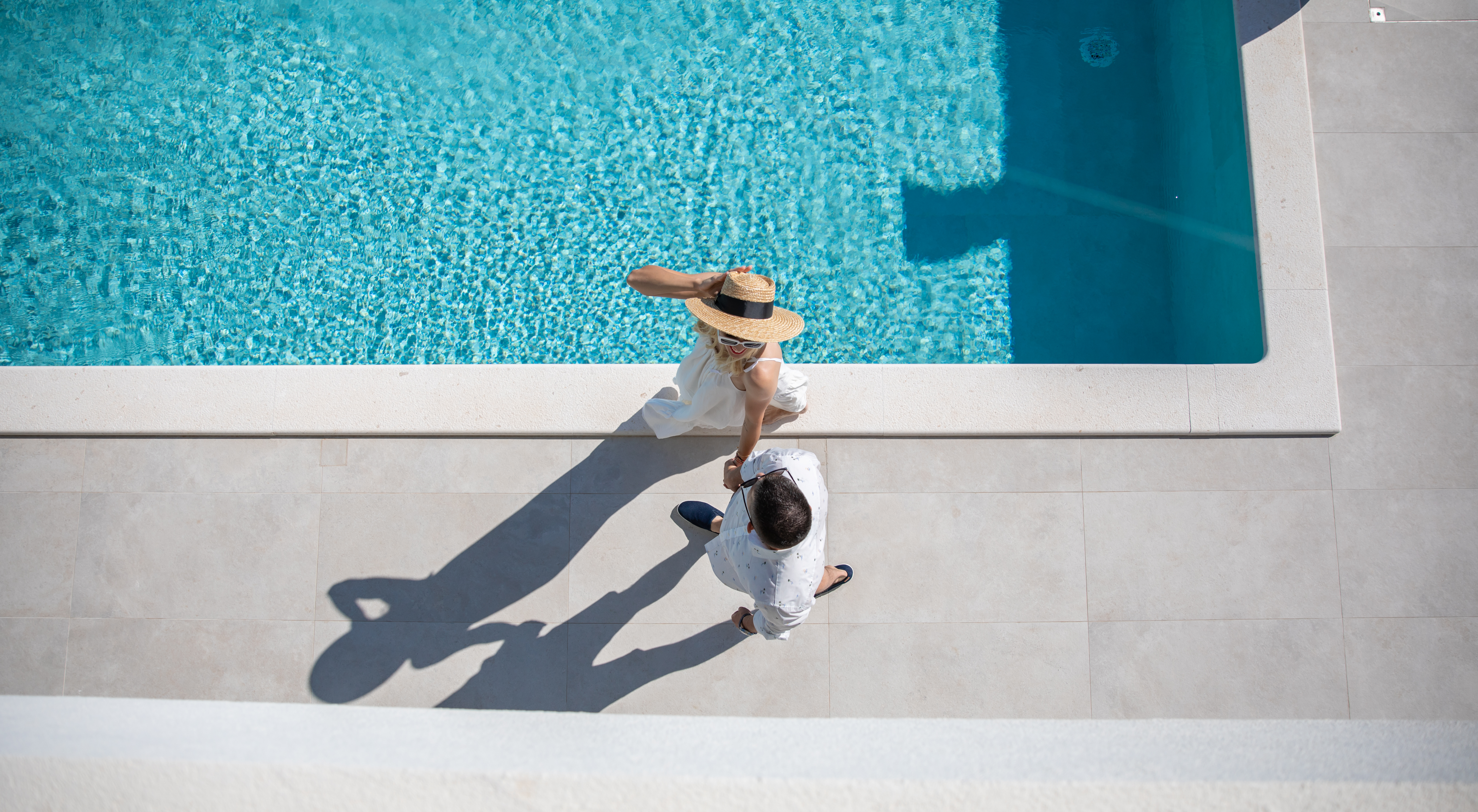 Overhead view of a couple walking hand in hand beside a crystal-clear private swimming pool at a luxury villa in Croatia, capturing a romantic summer getaway and elegant outdoor lifestyle.