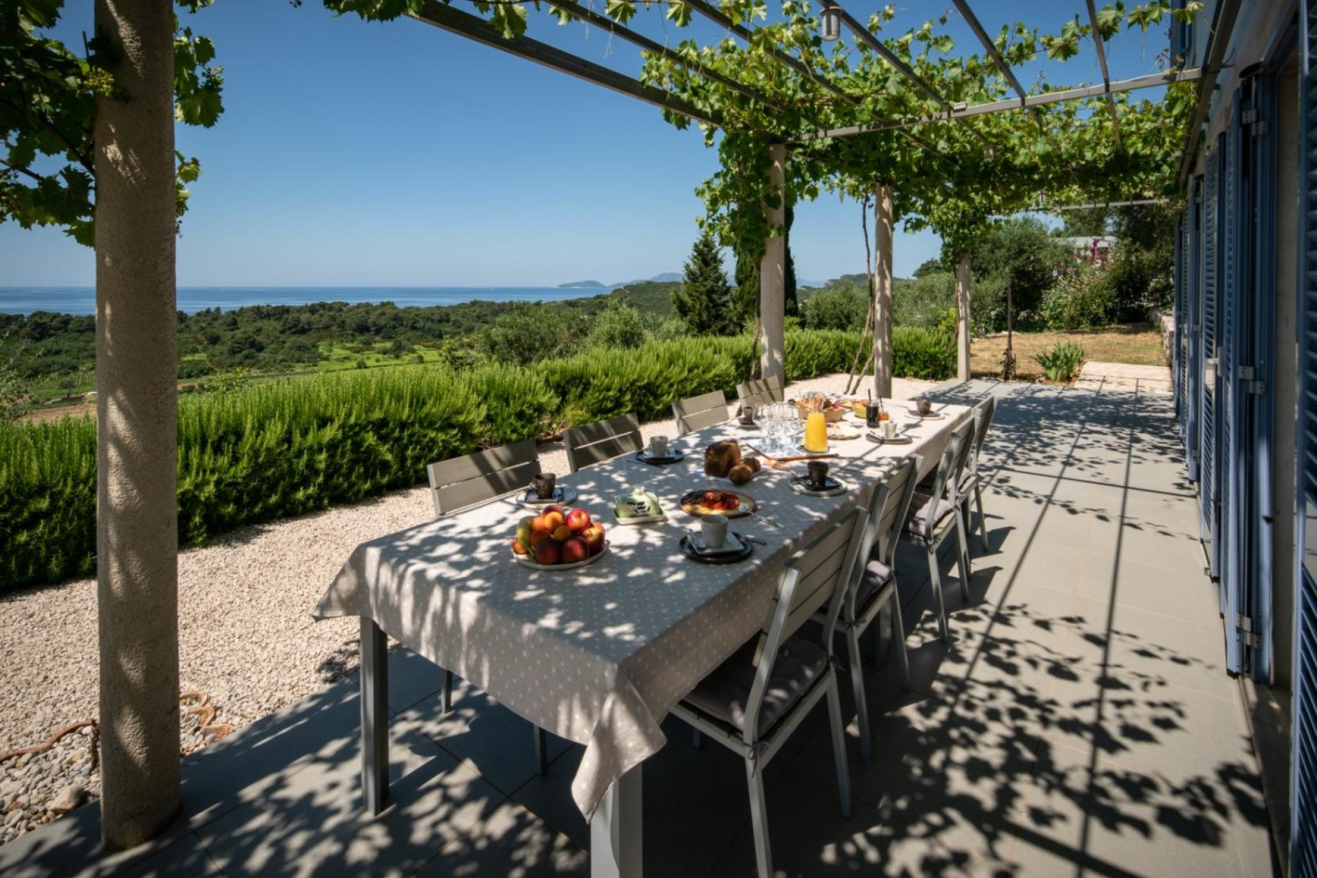 Shaded outdoor dining terrace at Villa Ella on Šipan, set beneath a vine-covered pergola with views of lush Mediterranean greenery and the Adriatic Sea.