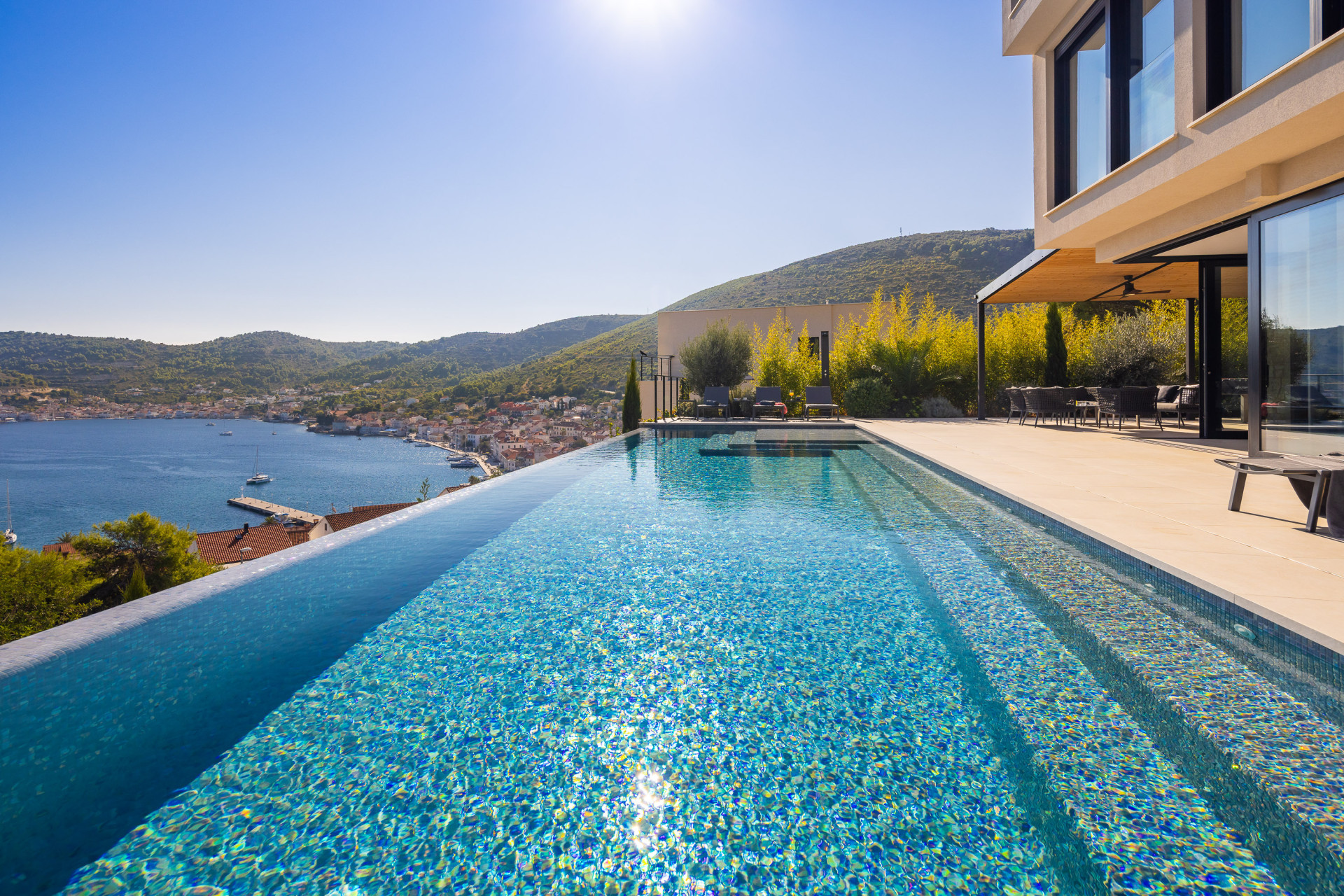 Villa Issa on Vis Island, featuring an infinity pool and spacious terrace with panoramic views over the Adriatic Sea and the coastal town below.