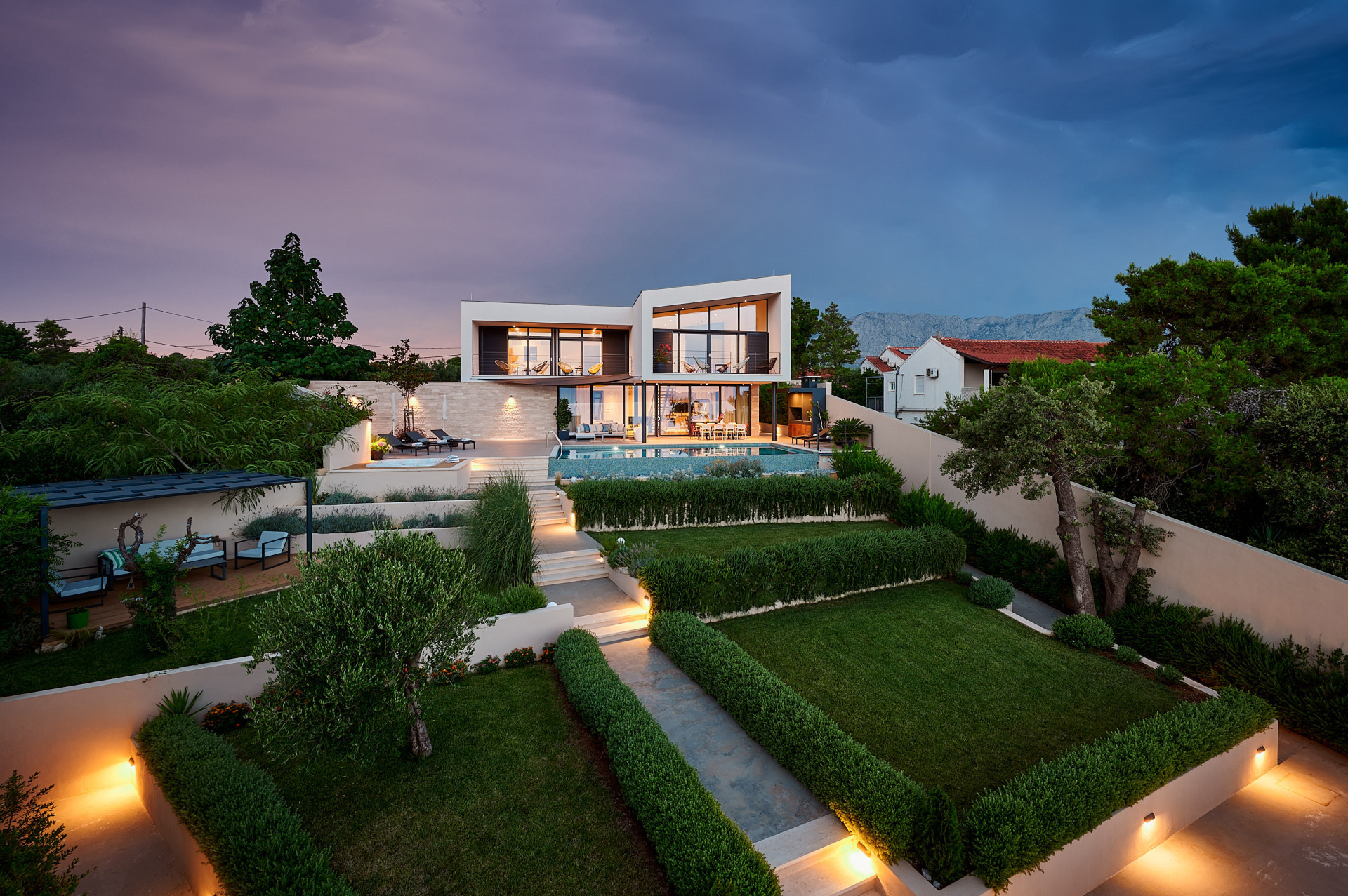 Villa Katina at dusk, featuring modern architecture, a private swimming pool, beautifully landscaped gardens and illuminated outdoor terraces.