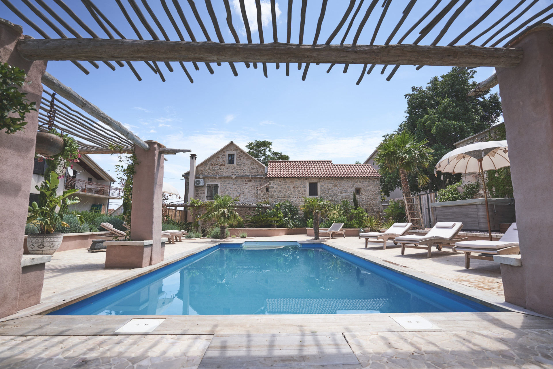Villa Oaza on Hvar Island featuring a private swimming pool, stone terrace with sun loungers, rustic wooden pergola and traditional stone house surrounded by Mediterranean greenery.
