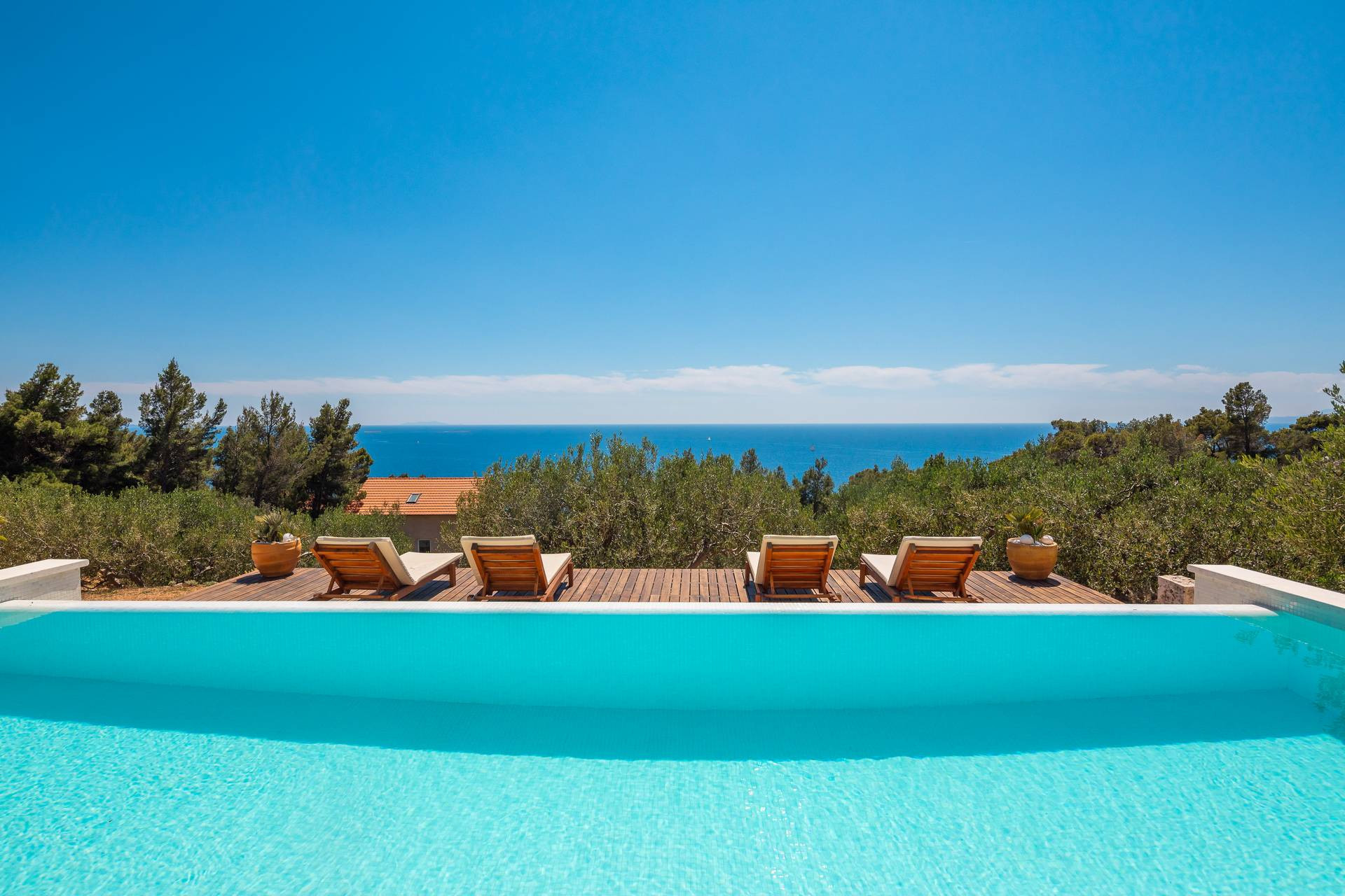 Villa Perka featuring an infinity pool, wooden sun loungers and a spacious terrace surrounded by Mediterranean greenery, with panoramic views of the Adriatic Sea.