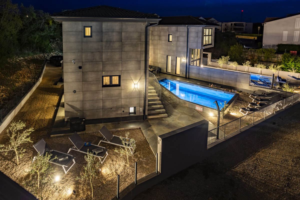 Moderna Villa Signature Krk con facciata in pietra di notte, con vista sull'area piscina e design esterno contemporaneo.