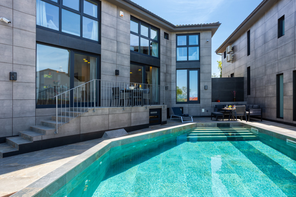 Lussuosa area piscina all'aperto presso Villa Signature Krk, con piscina privata turchese, sedute lounge e moderna architettura in pietra.