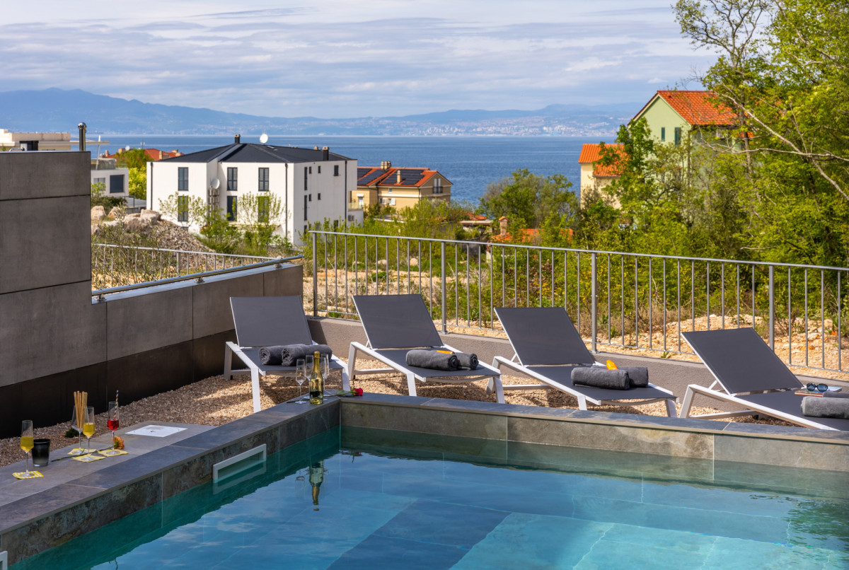 Soleggiata terrazza con piscina presso Villa Signature Krk, con moderni lettini, drink rinfrescanti a bordo piscina e vista panoramica sul mare.