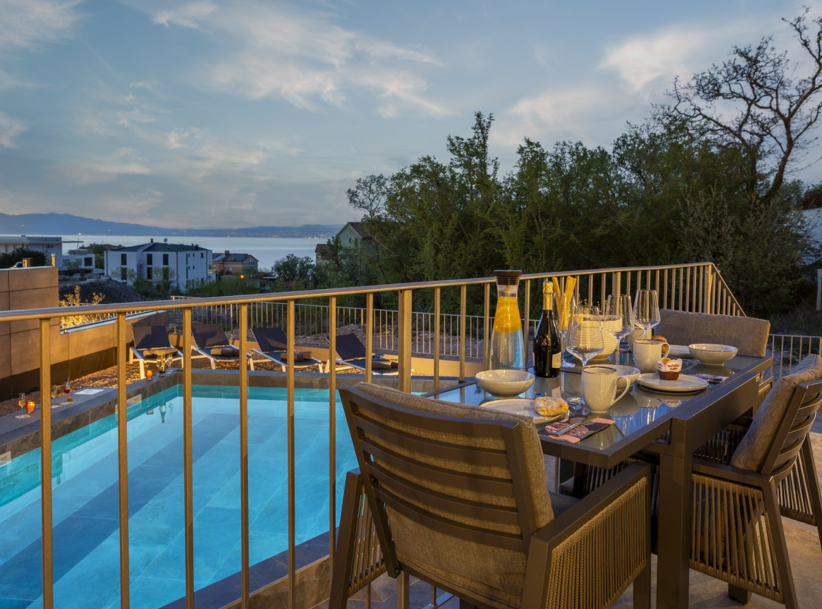 Elegante cena in terrazza presso Villa Signature Krk, con vista sulla piscina e sul mare Adriatico al tramonto.