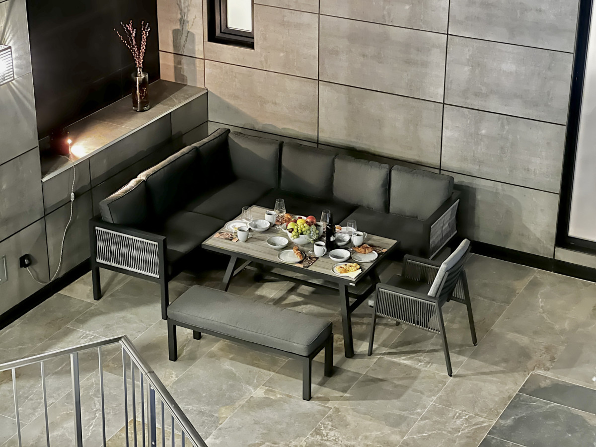 Elegante area lounge e zona pranzo all'aperto presso Villa Signature Krk, con un moderno divano ad angolo, pavimentazione in pietra e una tavola apparecchiata con cura.