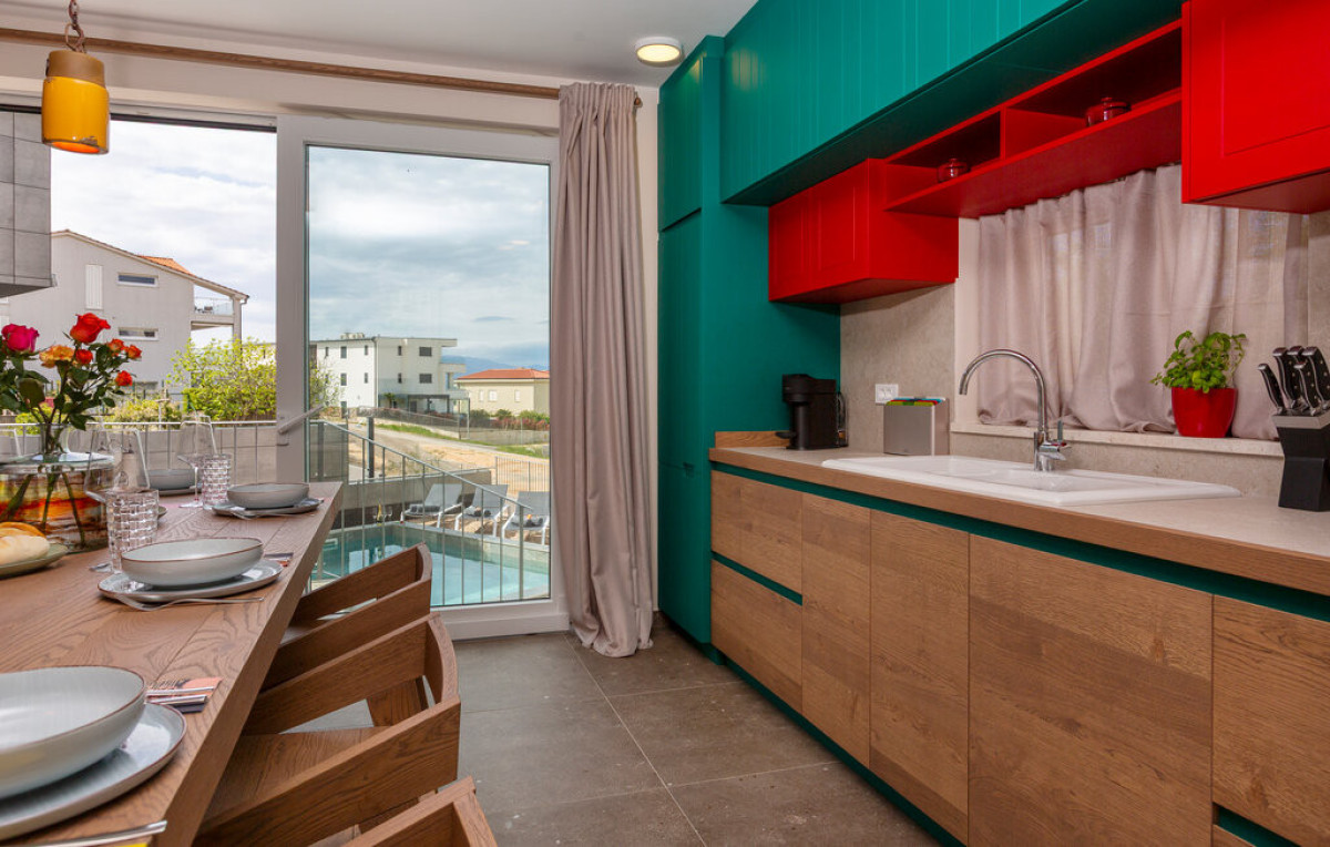 Cucina moderna completamente attrezzata presso Villa Signature Krk, con eleganti mobili in legno e verde petrolio e vista sulla piscina all'aperto.