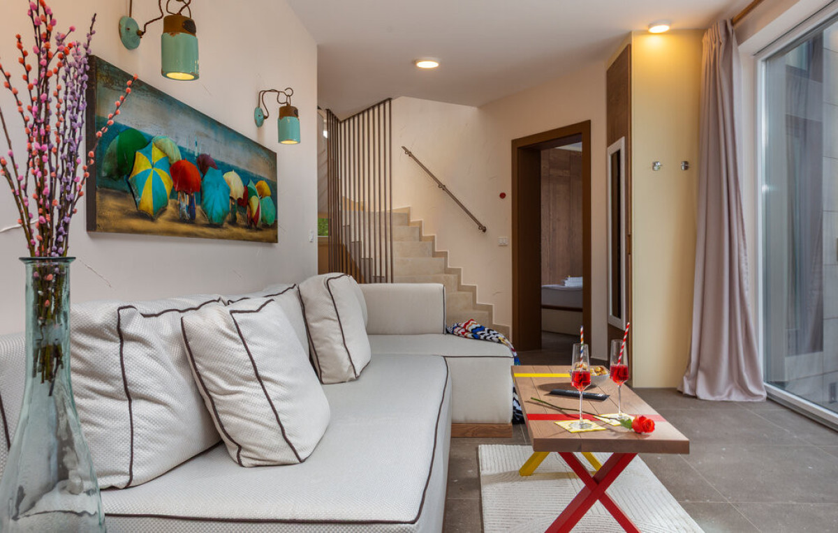 Accogliente angolo lounge a Villa Signature Krk, con un morbido divano, una decorazione murale artistica a tema spiaggia e un invitante spazio vicino alle scale.