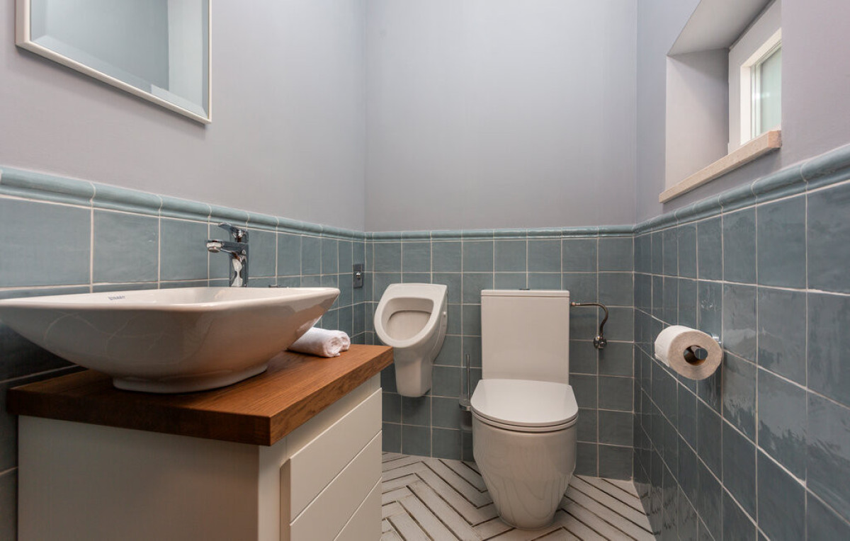 Moderno bagno di servizio presso Villa Signature Krk, con eleganti piastrelle blu, mobile lavabo in legno e orinatoio.