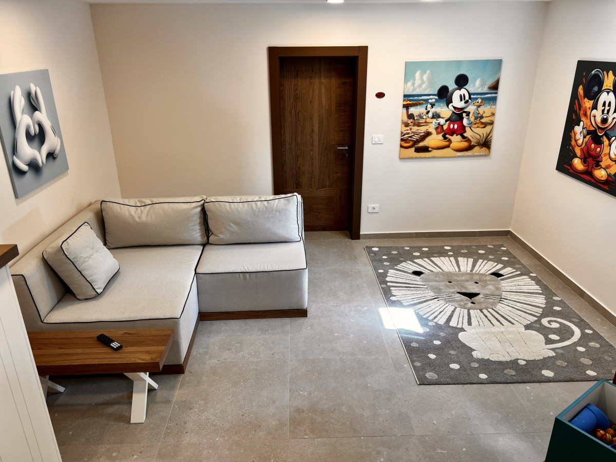 Divertente sala giochi per bambini presso Villa Signature Krk, con un comodo divano, un tappeto a tema leone e vivaci quadri di Topolino.