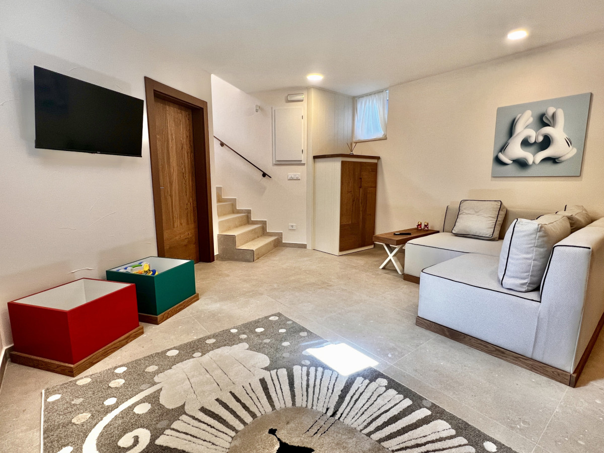 Spaziosa sala intrattenimento per bambini presso Villa Signature Krk, con TV a muro, scatole colorate per i giocattoli e una comoda area lounge.