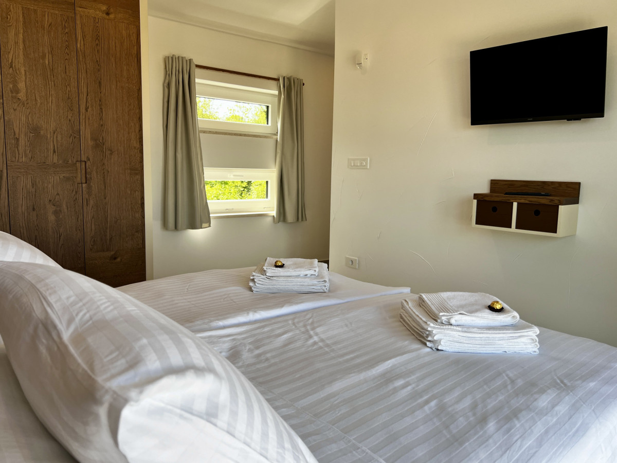Moderna camera da letto en-suite presso Villa Signature Krk, con TV a muro di fronte a un comodo letto matrimoniale e luce naturale.
