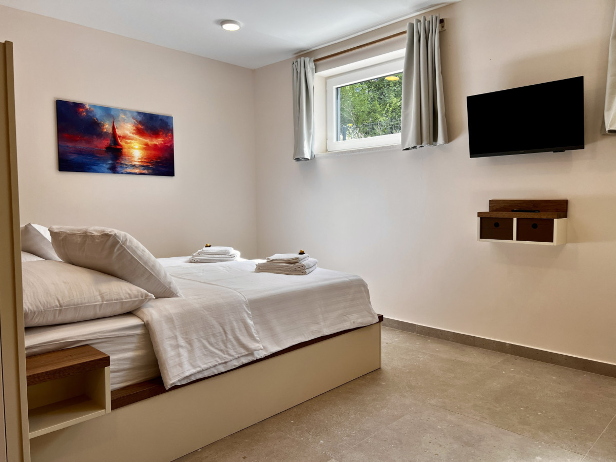 Rilassante camera da letto moderna presso Villa Signature Krk, con letto matrimoniale, TV a muro e quadro di un tramonto nautico.