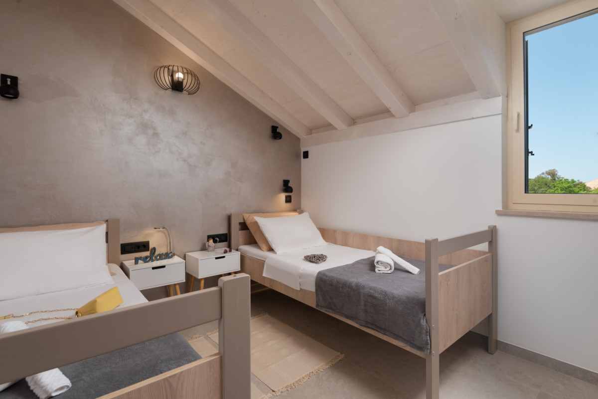 Loft-style twin bedroom in Villa Utopia with bright window overlooking the Mediterranean landscape.