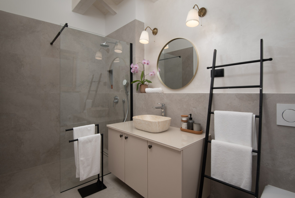 Modern bathroom with walk-in shower, stone sink, and black towel ladder