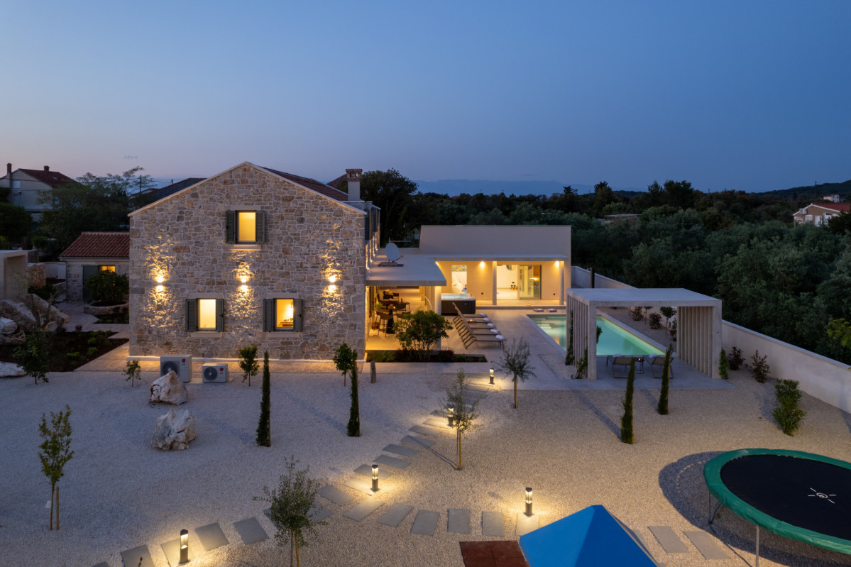 A stunning evening view of the lit stone residence, featuring the private pool and illuminated garden pathways on Ugljan.