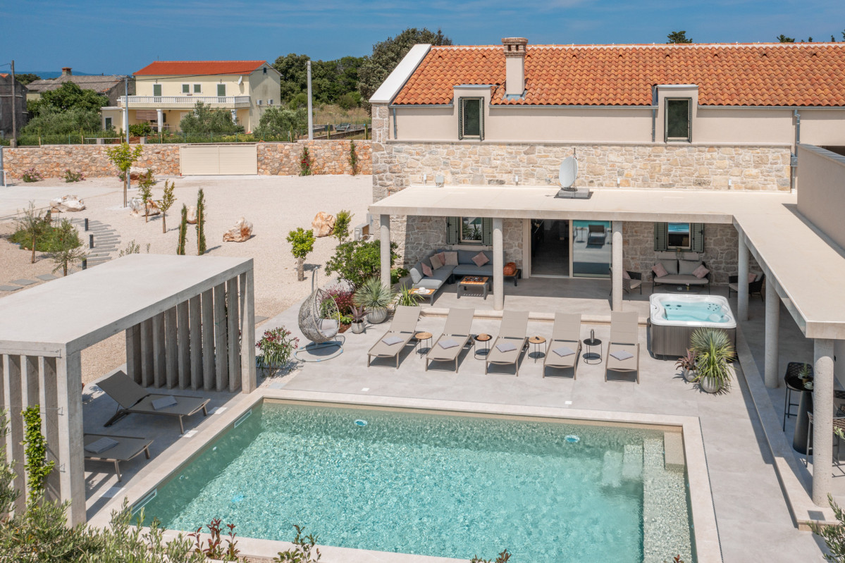 Exterior view of Villa Utopia with traditional stone walls and red tiled roof, overlooking a modern outdoor living space, private pool, and integrated sundeck area.