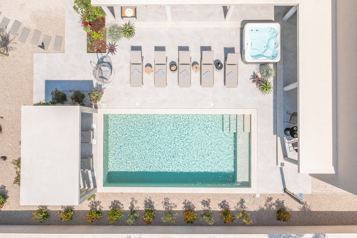 Aerial view of Villa Utopia’s sundeck, featuring a turquoise heated pool, luxury loungers, a hot tub, and a modern pergola in a minimalist Mediterranean setting.