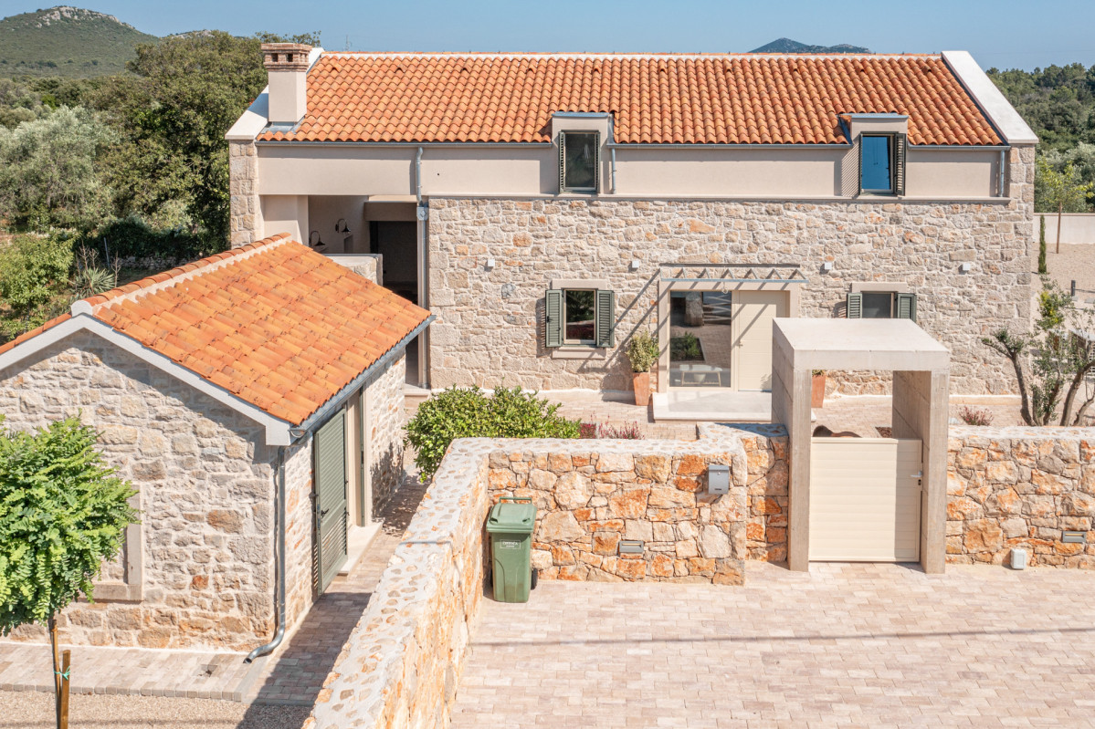 The elegant rear exterior and private paved driveway of Villa Utopia, showcasing the blend of rustic stone and modern island design.