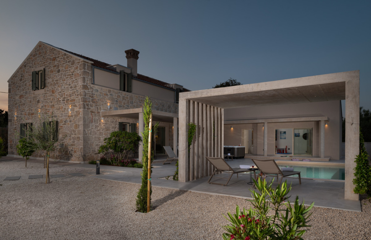 An elegant evening glow over the poolside cabana, modern sun loungers, and the illuminated stone facade of luxury villa Utopia.