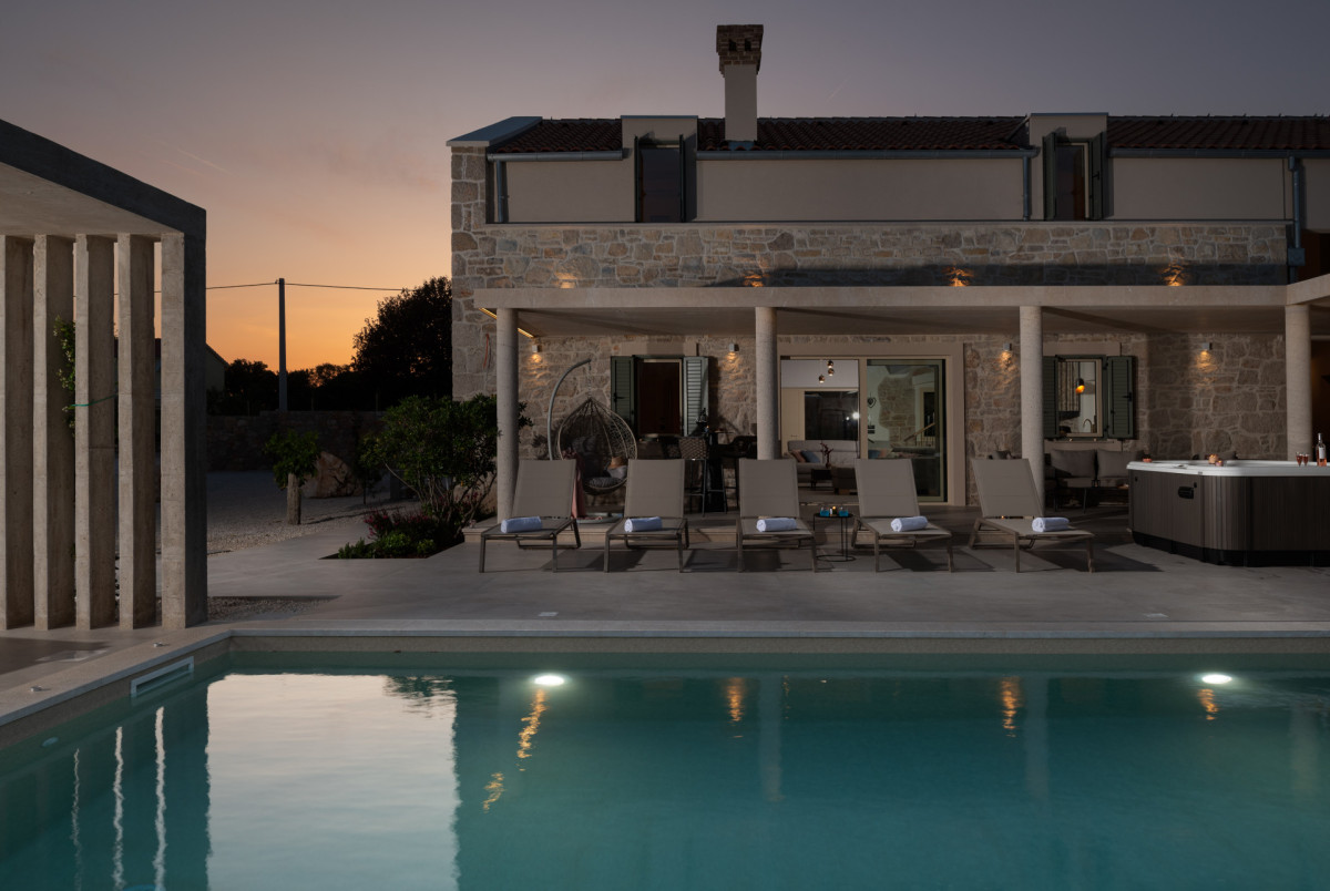 Serene sunset views over the illuminated pool, modern sun loungers, and luxurious outdoor spa area on Ugljan.