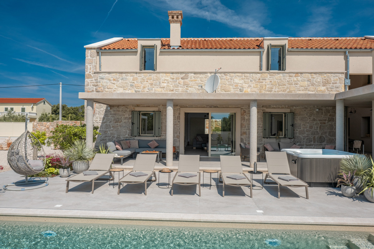Poolside terrace at Villa Utopia, featuring a row of modern beige sun loungers, a grey L-shaped sofa, and a private jacuzzi under a traditional stone-and-tile structure on Ugljan.