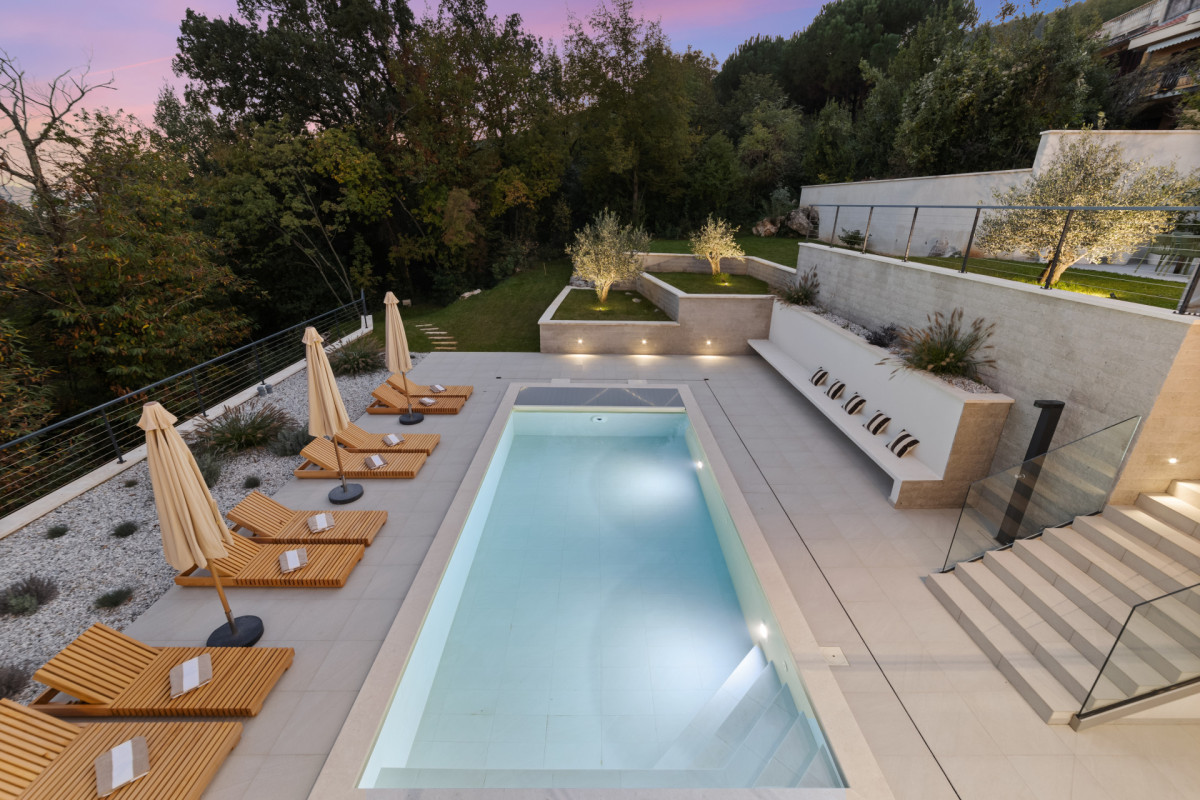 Moderne Poolarchitektur der Villa Casa Calme: ein klarliniger Swimmingpool, umgeben von Steinfliesen, gepflegtem Grün und gemütlichen Lounge-Sitzgelegenheiten.