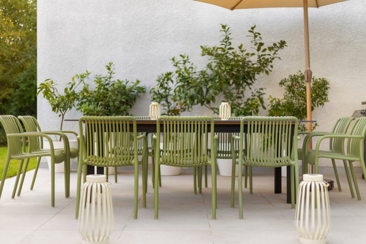 Nahaufnahme des Essbereichs im Freien in der Villa Casa Calme mit stilvollen olivgrünen Stühlen, dekorativen Laternen und üppigen mediterranen Pflanzen im Hintergrund.