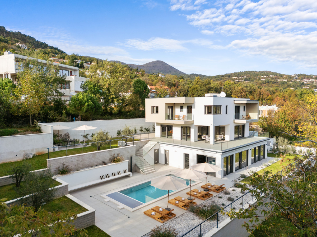 Luftaufnahme der luxuriösen Villa Casa Calme, die ihre moderne, mehrstöckige Architektur, den privaten Swimmingpool, die großzügigen Sonnenterrassen und die üppige mediterrane Hügellandschaft zeigt.