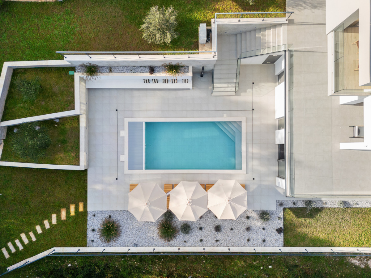 Luftaufnahme der privaten Poolanlage der Villa Casa Calme direkt von oben, mit einem modernen türkisfarbenen Swimmingpool, eleganten Sonnenschirmen und sorgfältig angelegten mediterranen Gärten.