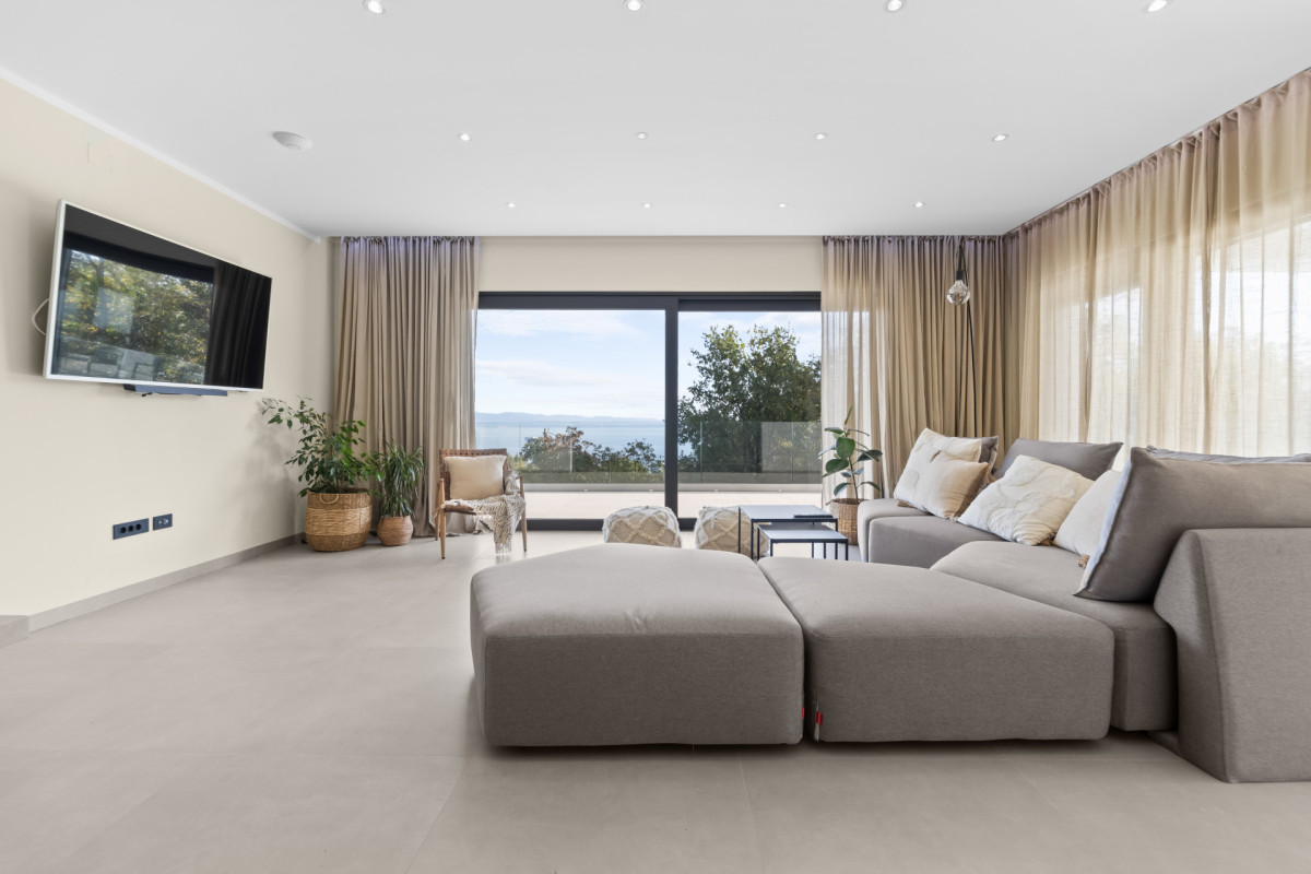 Helles und geräumiges Wohnzimmer in der Villa Casa Calme mit einem großen, gemütlichen Sofa, einem wandmontierten Fernseher und einer Glasschiebetür s mit atemberaubendem Meerblick.