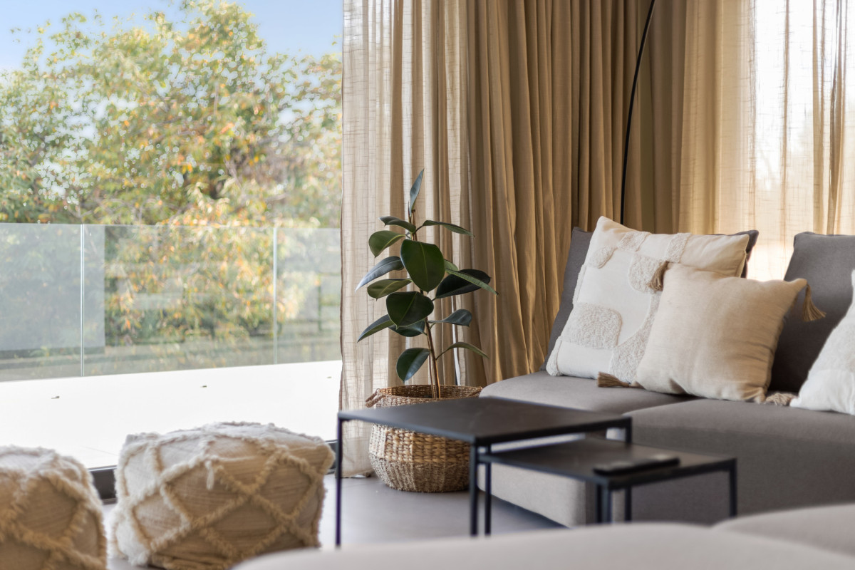 Modernes Lounge-Dekor in der Villa Casa Calme: ein modulares graues Sofa sa Kissen im Boho-Stil, schwarze Satztische und luftige Vorhänge, die eine friedliche Atmosphäre schaffen.
