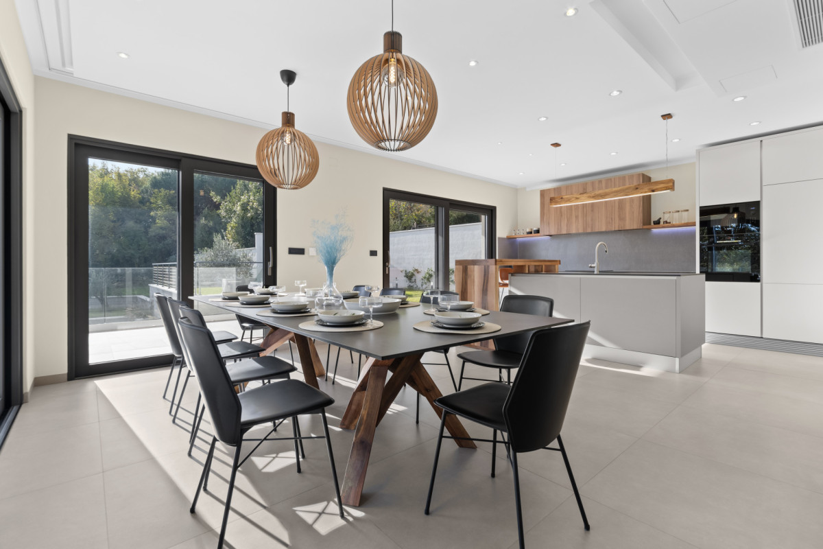 Heller und luftiger Ess- und Küchenbereich in der Villa Casa Calme: zeitgenössische Möbel, Designer-Holzlampen und große Glastüren mit Blick in den Garten.