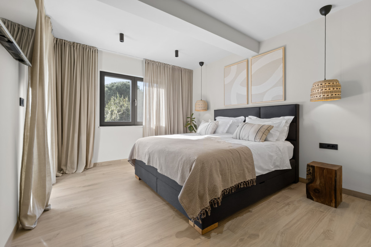 Helles und geräumiges Hauptschlafzimmer in der Villa Casa Calme mit minimalistischer Kunst, raumhohen Vorhängen und Akzenten aus Naturholz für einen erstklassigen Urlaubsaufenthalt.