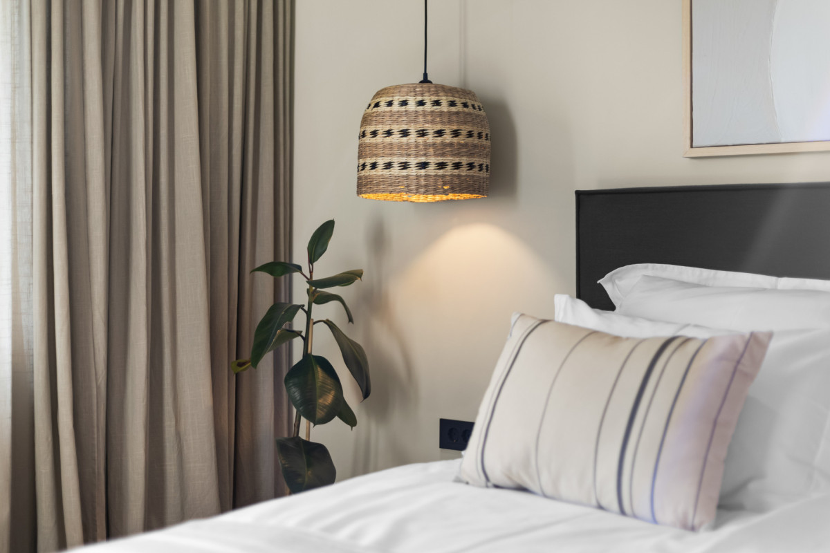 Eine Hängelampe aus Naturfasern, ein minimalistisches Kopfteil und eine Topfpflanze, die das elegante Innendesign der Villa Casa Calme unterstreichen.