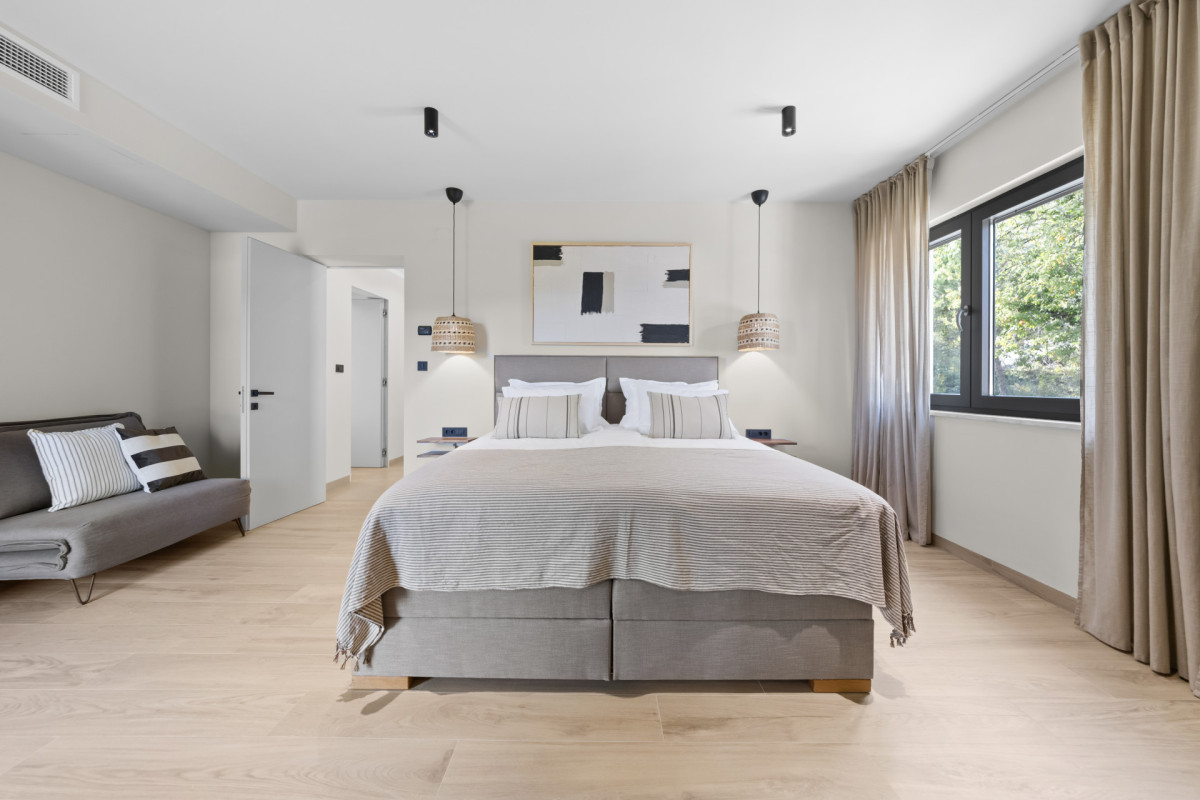 Symmetrische Ansicht eines großzügigen Hauptschlafzimmers in der Villa Casa Calme mit einem King-Size-Bett, einem zusätzlichen Schlafsofa, moderner abstrakter Kunst und warme